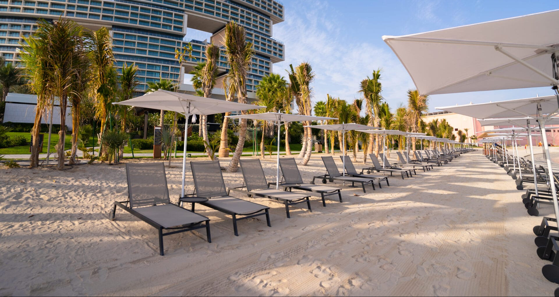Beachside_resort_with_rows_of_modern_aluminum_sun_loungers_and_white_umbrellas_by_Moss_Timber_set_against_a_luxury_architectural_backdrop.